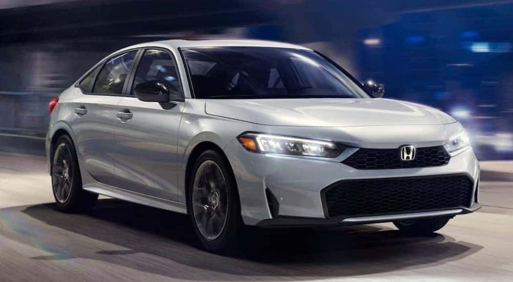 A white 2025 Honda Civic Sport Hybrid is shown driving at night.