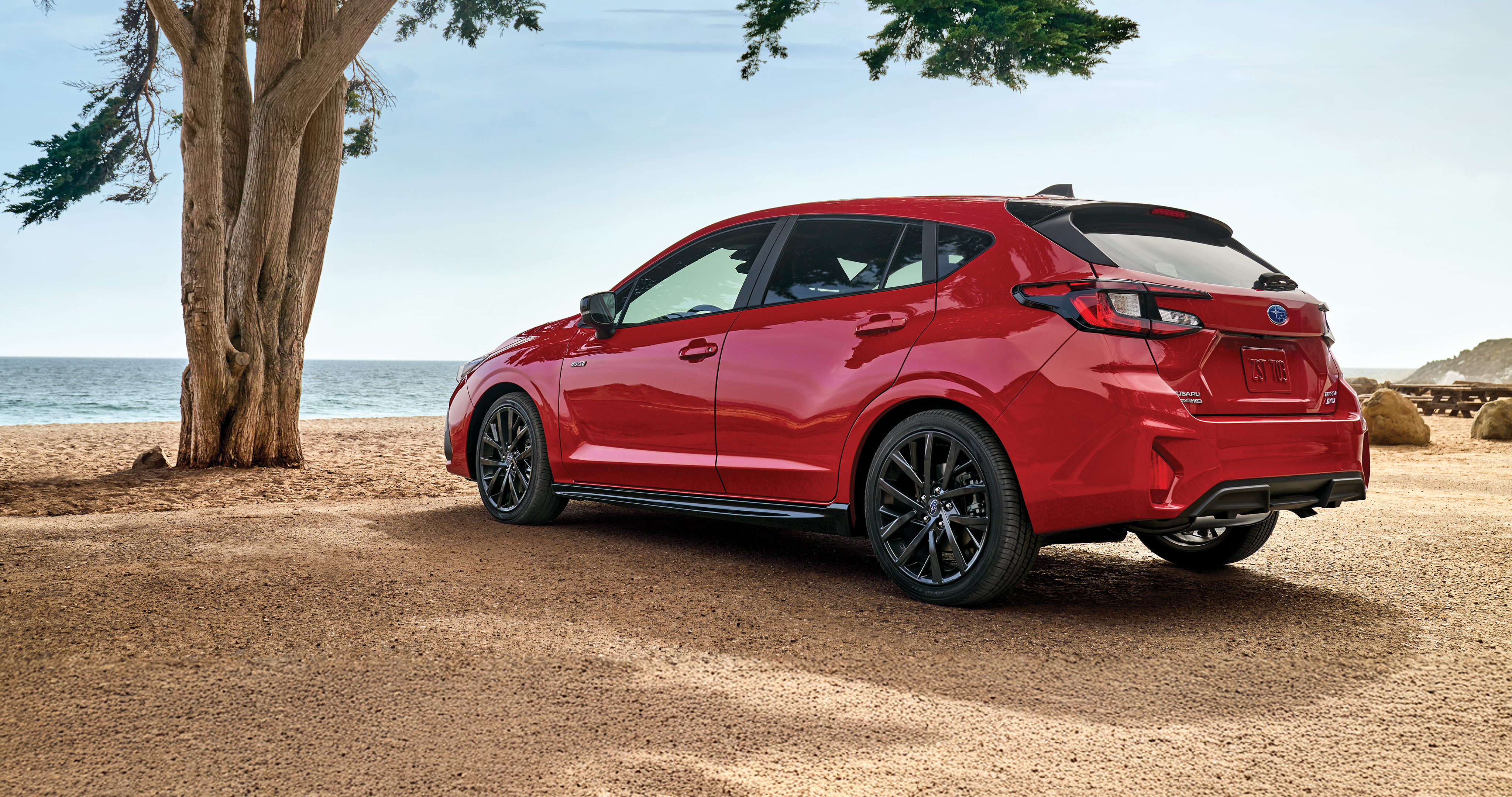 25_IMP_gallery_position_1.png / A red Impreza AWD hatchback parked by the ocean.