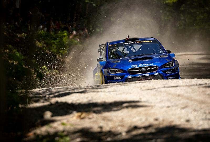 Blue Subaru WRX rally car kicking up gravel on a forest stage