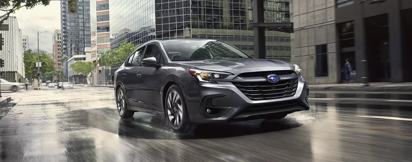 A gray 2024 Subaru Legacy Limited driving a wet city road.