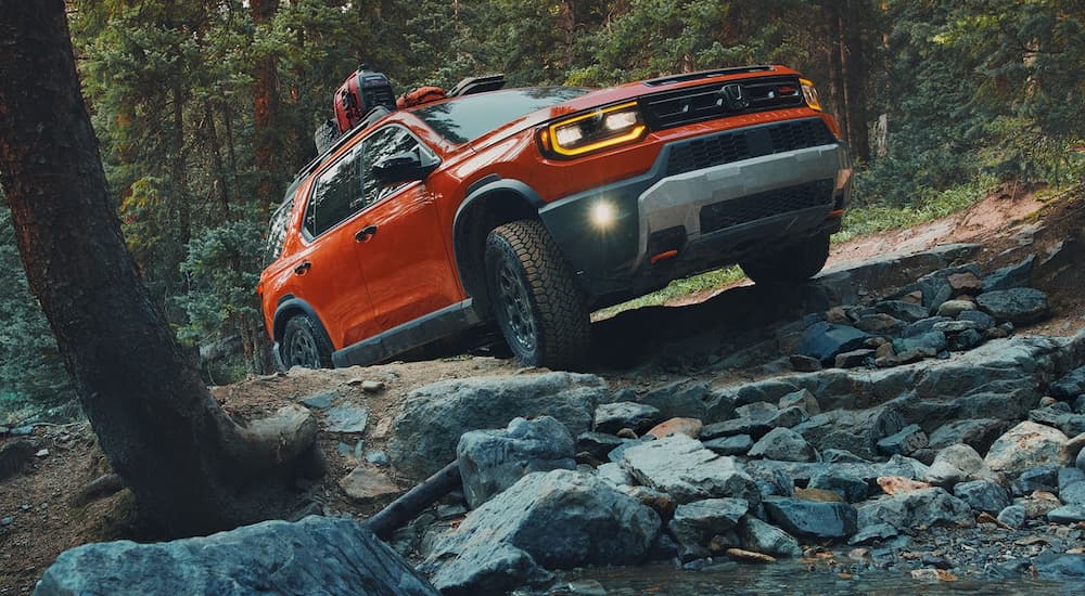 Orange 2026 Honda Passport driving off-road up a hill.