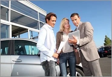 Salesperson showing a couple paperwork beside a silver car