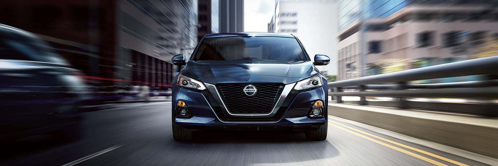 Blue Nissan Altima sedan driving down a city street