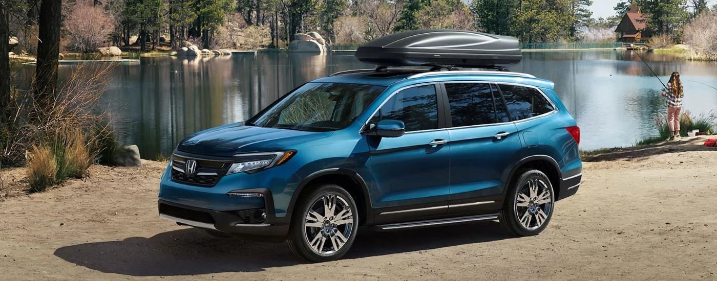 A blue 2021 Honda Pilot is shown from the side on a lakeshore.