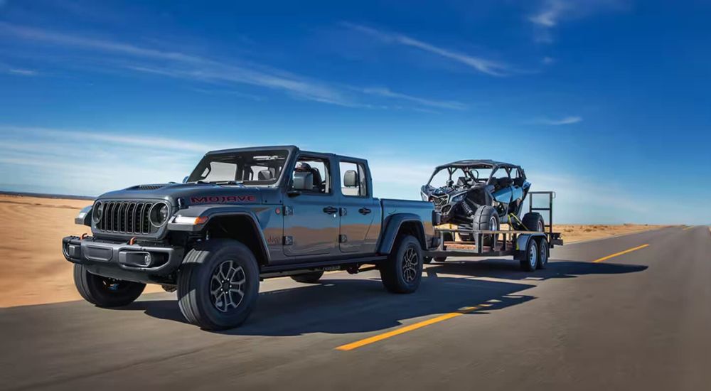 A silver 2024 Jeep Gladiator Mojave is shown towing an ATV.