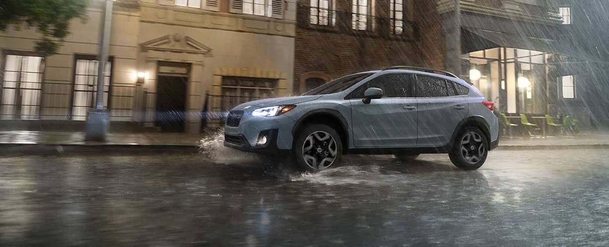 Subaru Crosstrek driving on a rainy city street at night