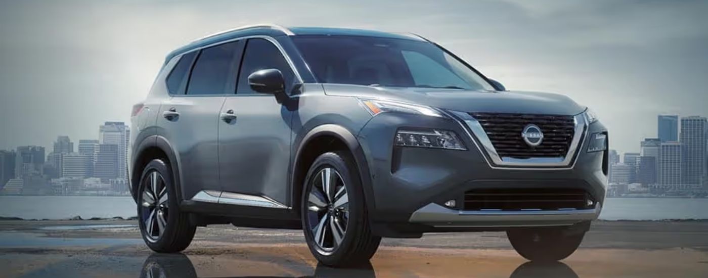 A silver 2024 Nissan Rogue parked in front of a city skyline.