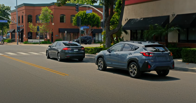 A Subaru stopped behind another car at an intersection.