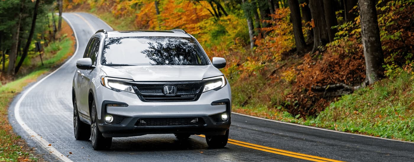 A white 2021 Honda Pilot Black Edition is driving down a winding road.