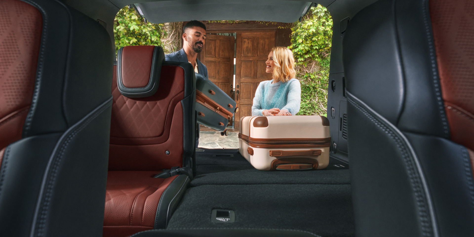 Rear cargo area of the 2027 INFINITI QX80 with folded third-row seats, Sepia Brown quilted leather second-row seats, and luggage being loaded through the open liftgate.