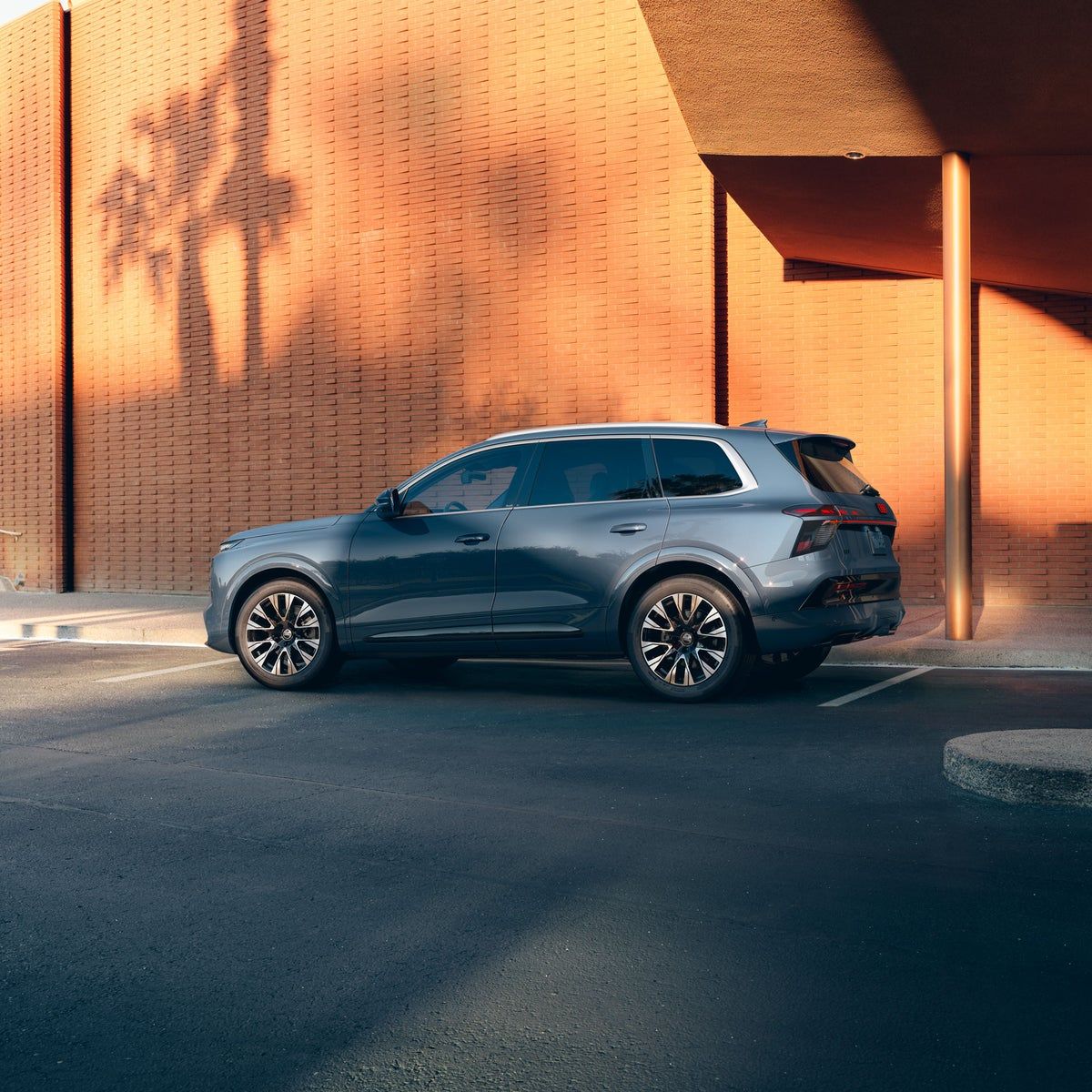 2027 Audi Q7 three-row luxury SUV in profile beside a sunlit brick wall