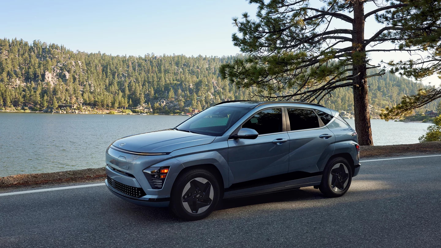 Side view of the Hyundai Kona EV parked by a lake with a scenic forest backdrop