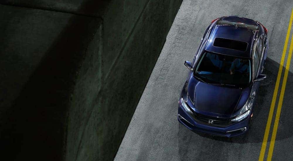 A dark blue 2021 Honda Civic is shown from high angle driving past a concrete wall.