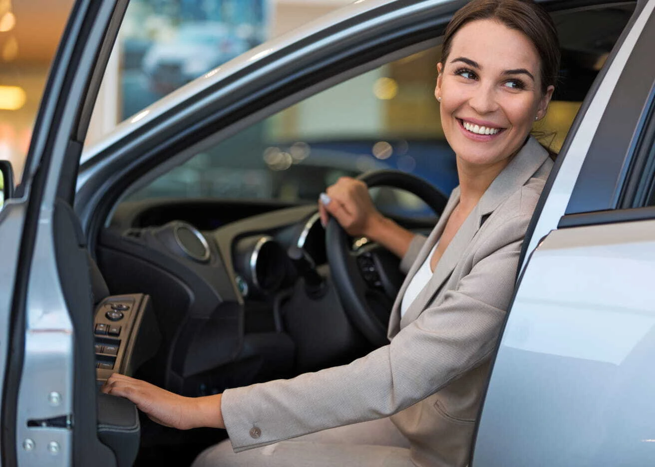 Smiling woman sitting in the driver’s seat of a vehicle with the door open inside a dealership.