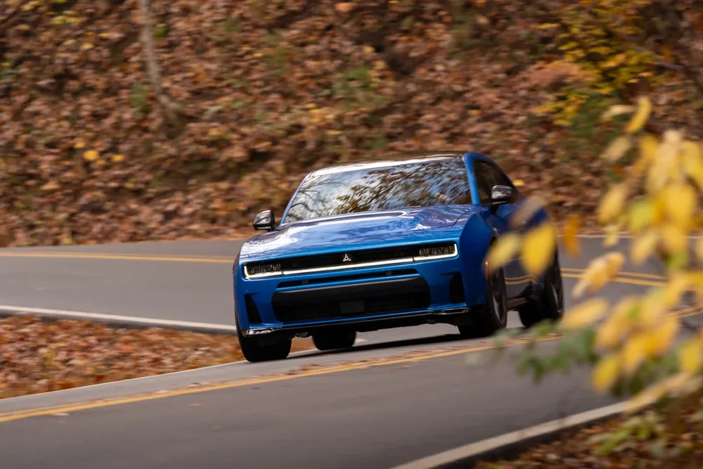 A blue SUV driving along a winding road surrounded by autumn foliage.