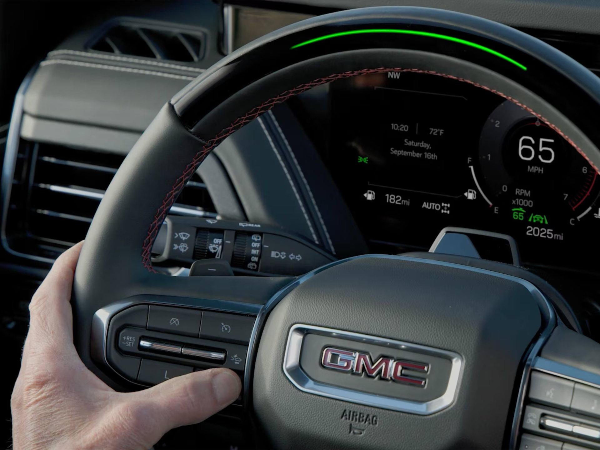Driver’s hand on a GMC Yukon steering wheel with the green Super Cruise light bar lit