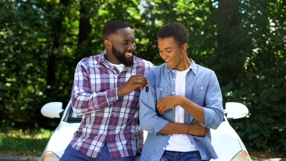 smiling dad hands car keys to teenage son