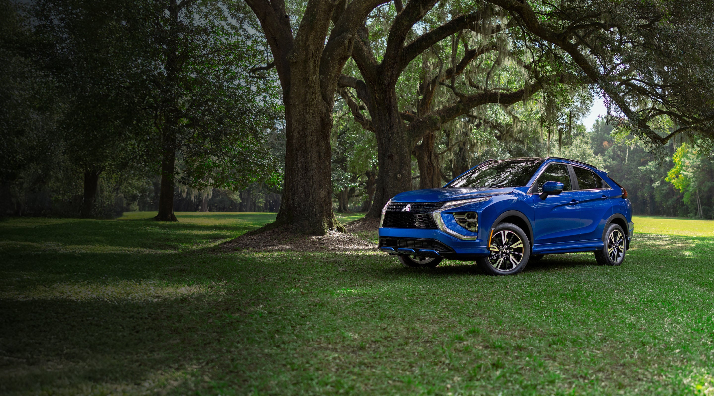 2026 blue Mitsubishi Eclipse Cross parked in grassy field with tall trees in background