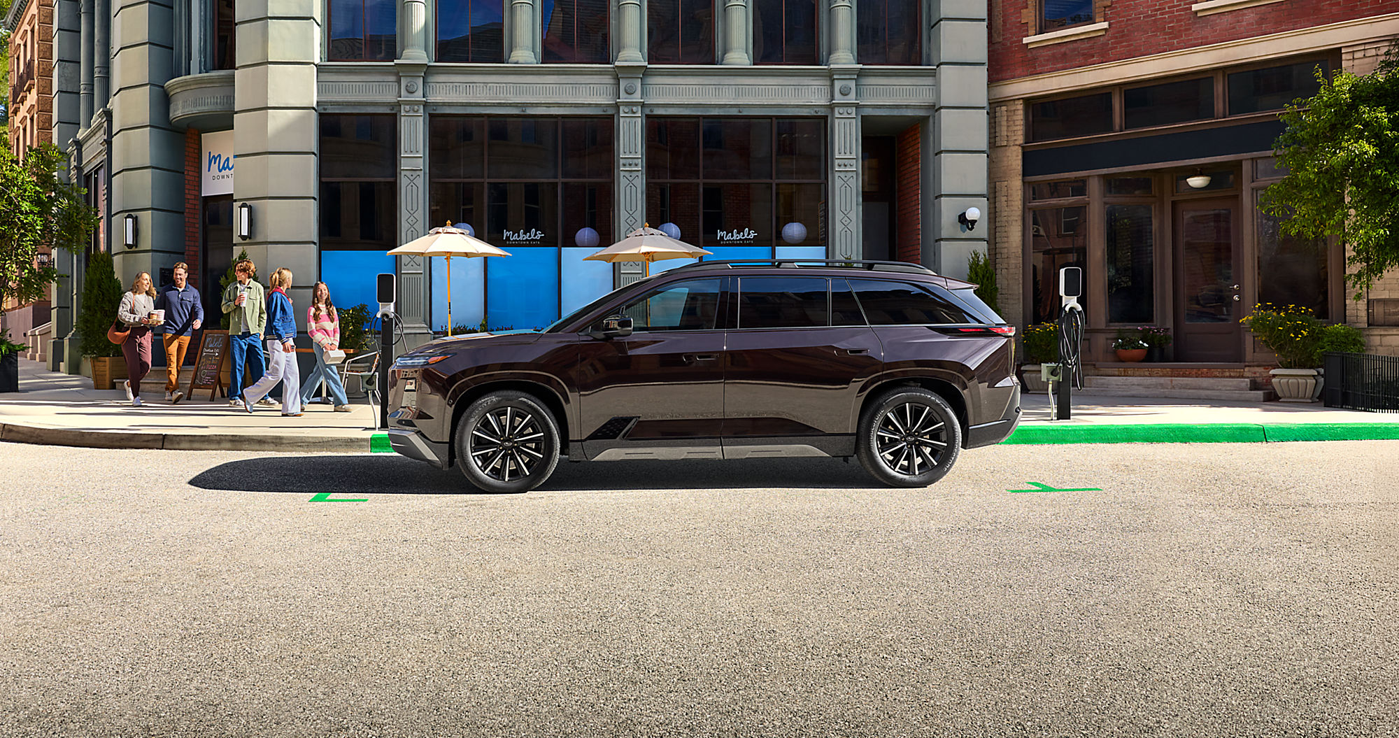 2027 Subaru Getaway in dark maroon charging on a city street, side profile view