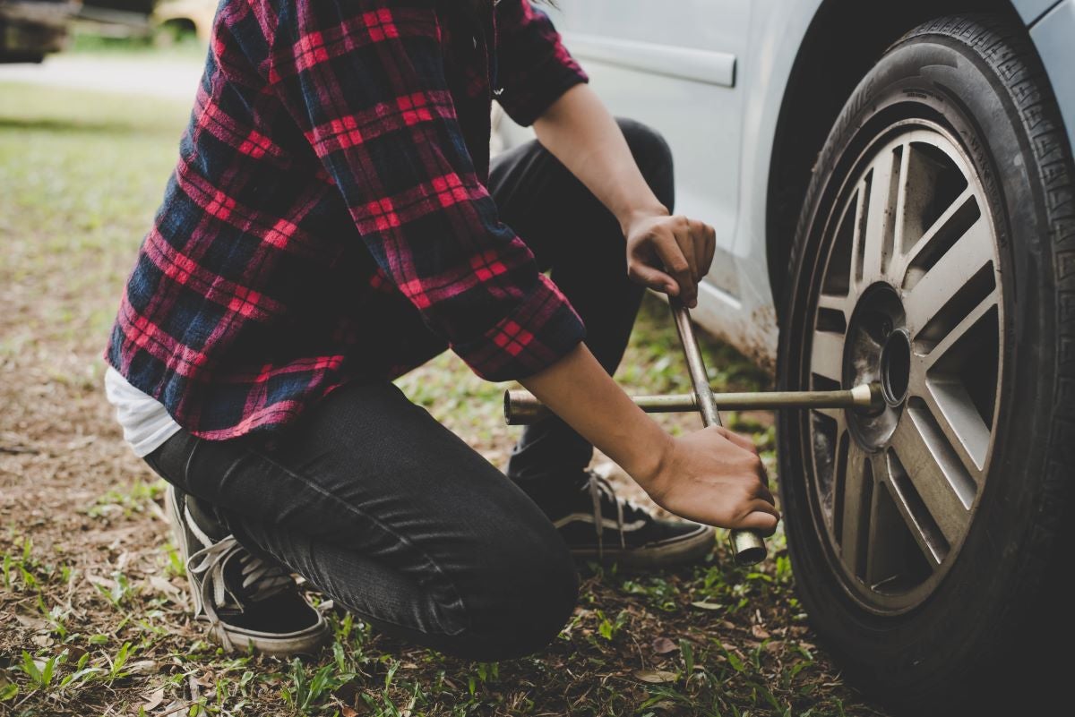 Person using a lug wrench to loosen the lug nuts on a car tire