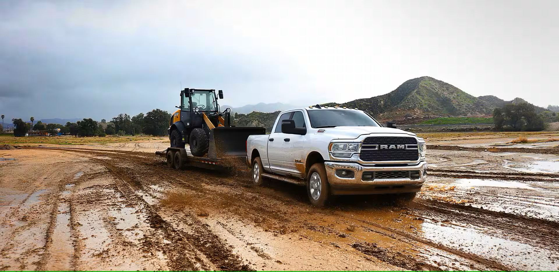 A white truck driving in the mud with a trailer.
