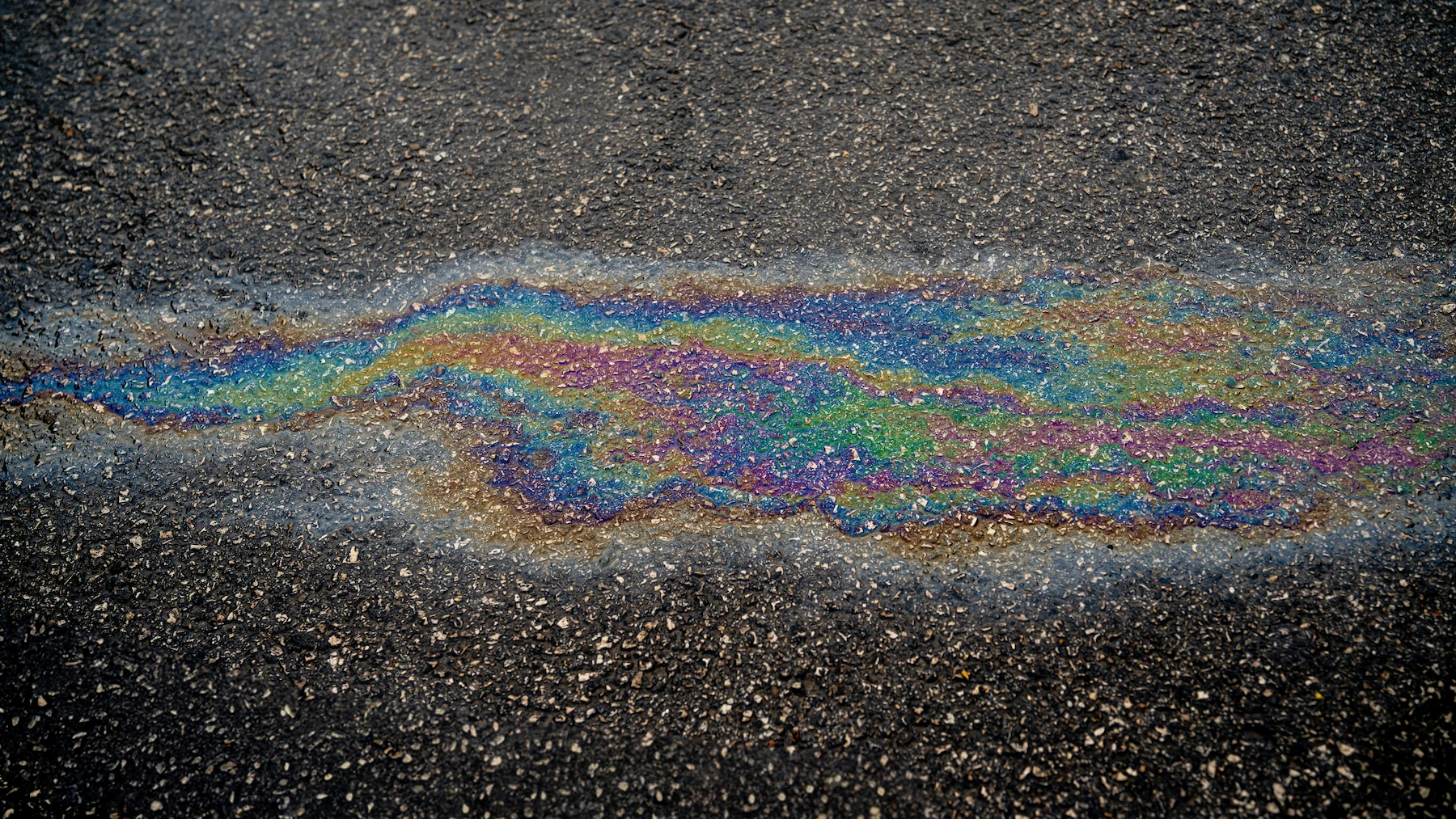Rainbow-colored oil stain on pavement, representing a vehicle oil leak that a certified technician can diagnose and repair