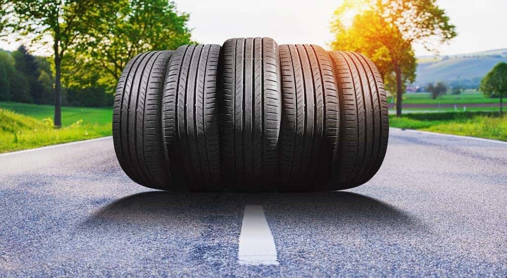 Five tires are shown lined up on a road on a sunny day.