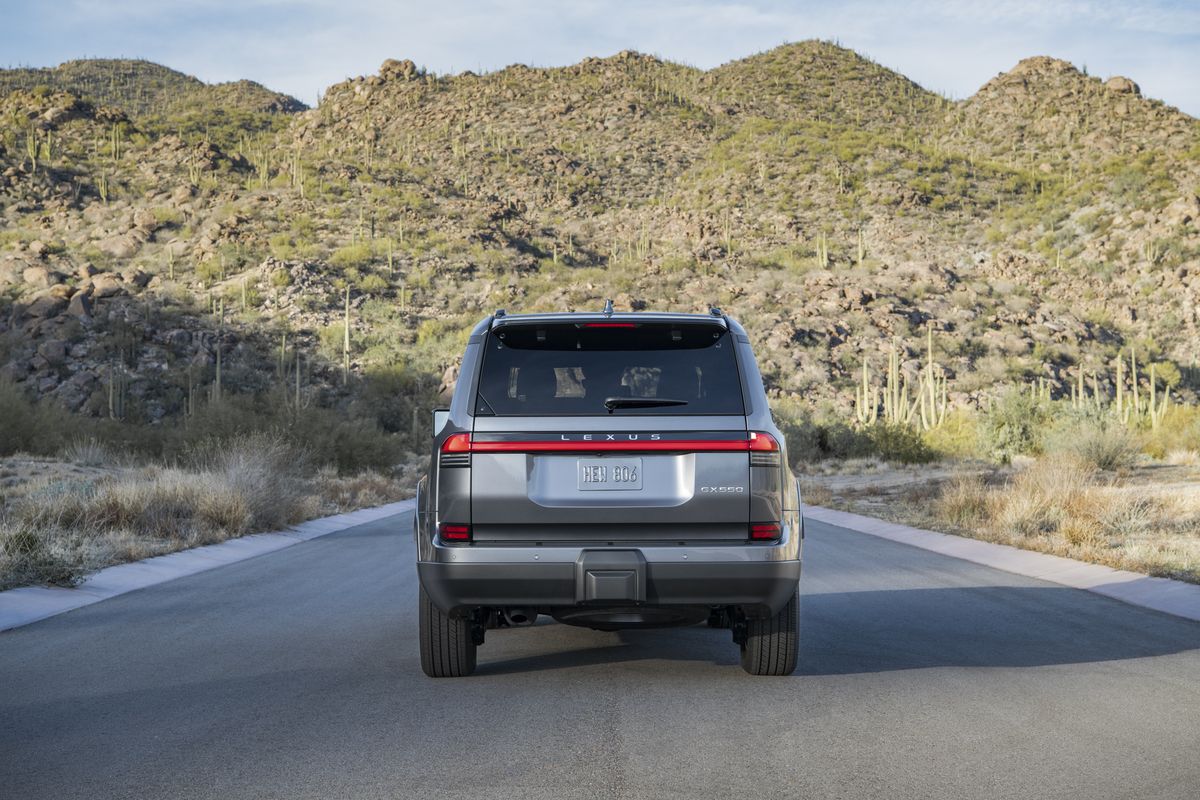 2026 Lexus GX rear view driving on a paved road through desert mountains