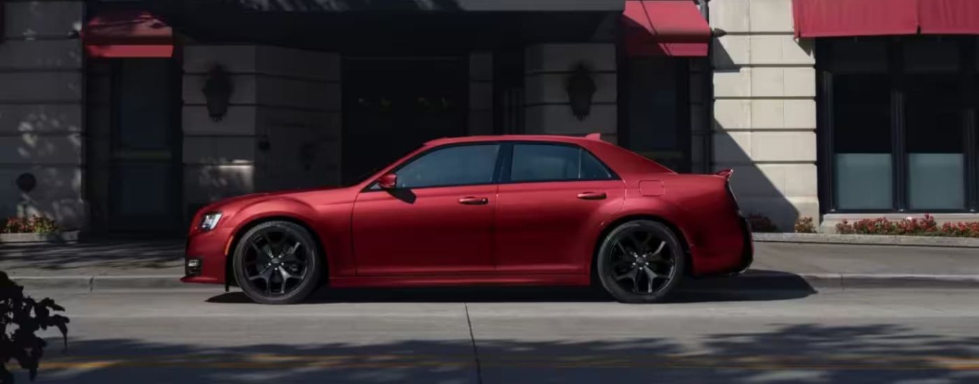 A red 2023 Chrysler 300 is shown from the side in front of a concrete wall.