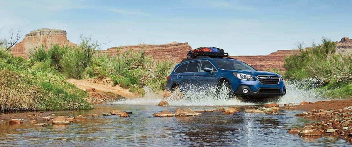 Blue Subaru Outback splashing through a shallow creek
