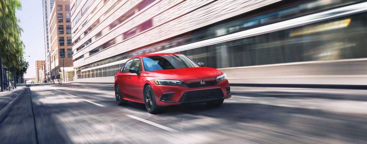 Red 2023 Honda Civic Sport driving though a city