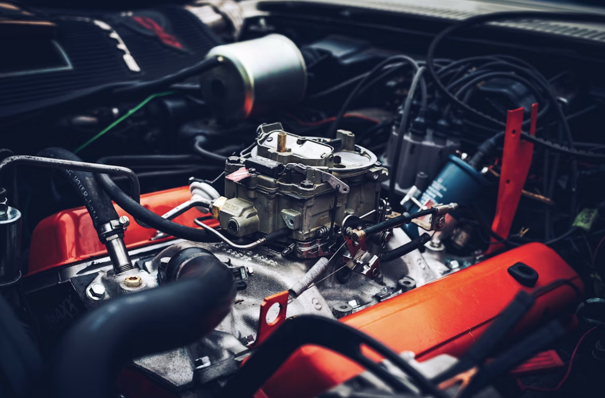 Close-up view of a carburetor mounted on a classic car engine with bright red valve covers.