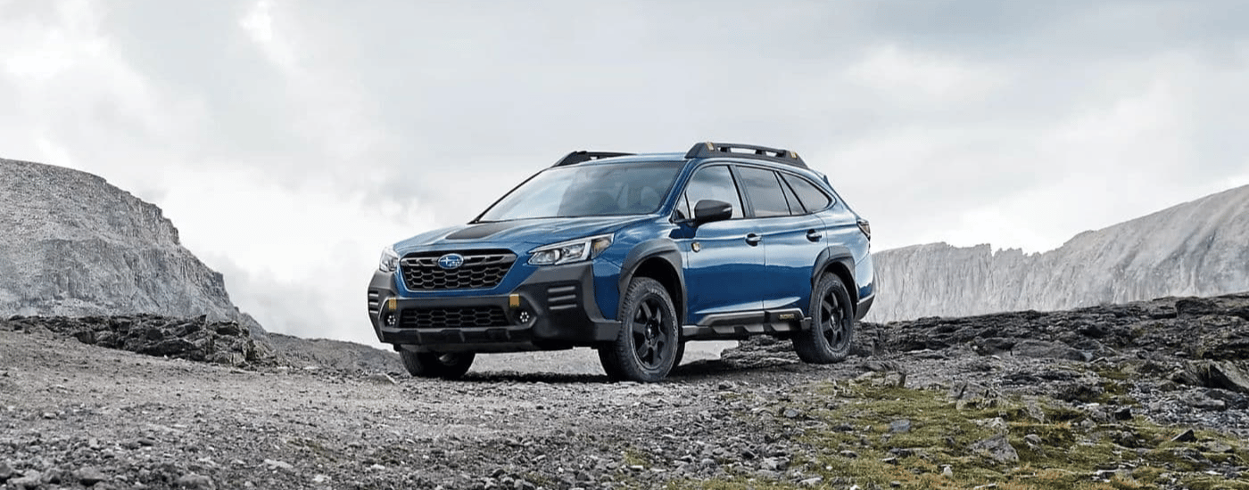 A blue 2023 Subaru Outback Wilderness is shown parked on a mountain path.