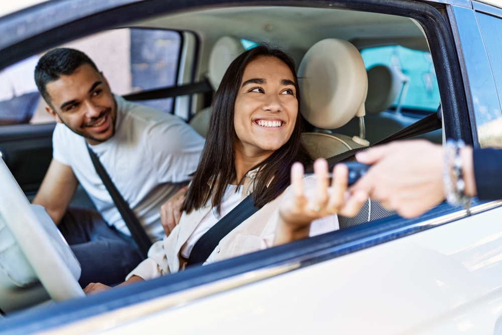 Young hispanic couple driving auto at the city. Girl smiling happy holding key of new car.