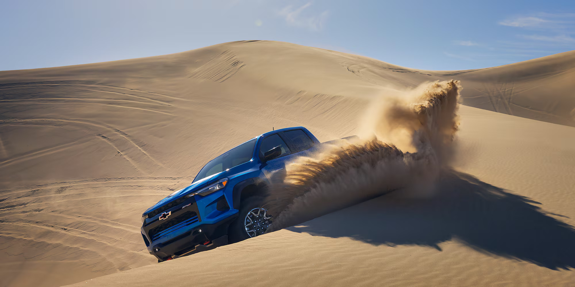 A blue truck driving in the sand.