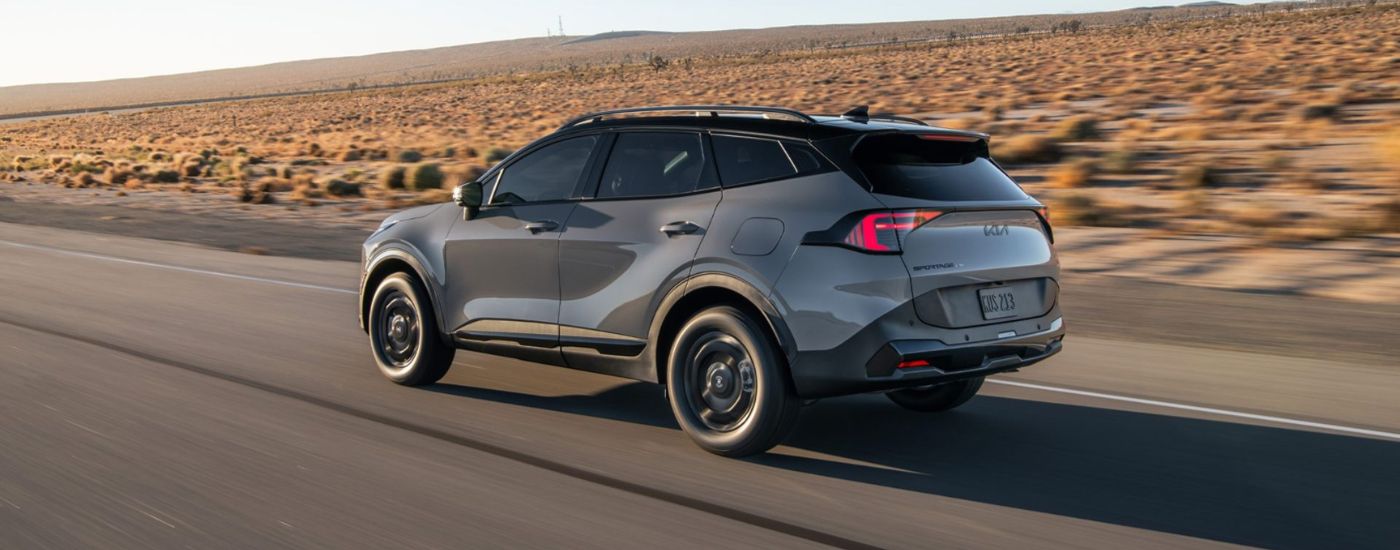 Rear view of a grey 2026 Kia Sportage driving on a paved road.