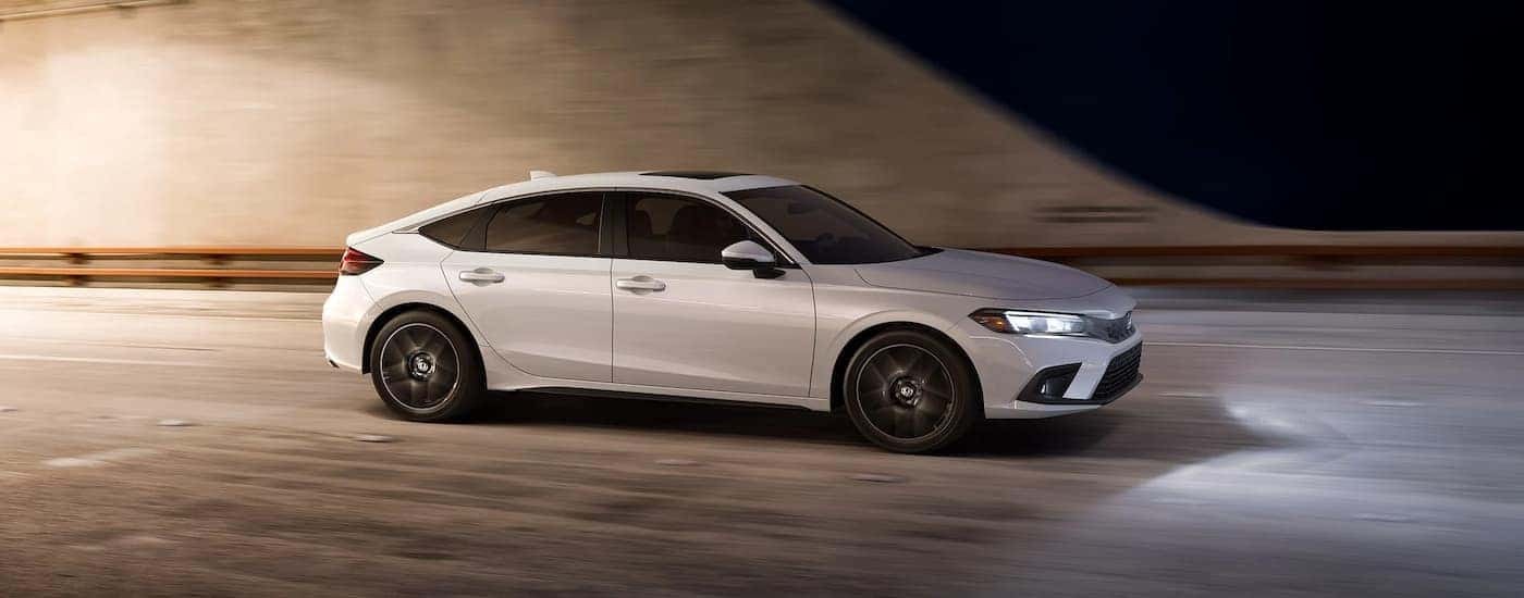 A white 2022 Honda Civic Hatchback is shown from the side driving through a tunnel.