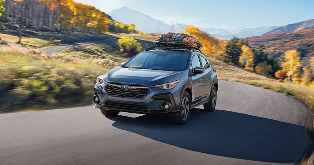 Gray 2025 Subaru Crosstrek with a roof cargo box driving on a mountain road