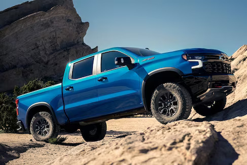 A Blue 2024 Chevrolet Silverado climbing sandstone rocks.