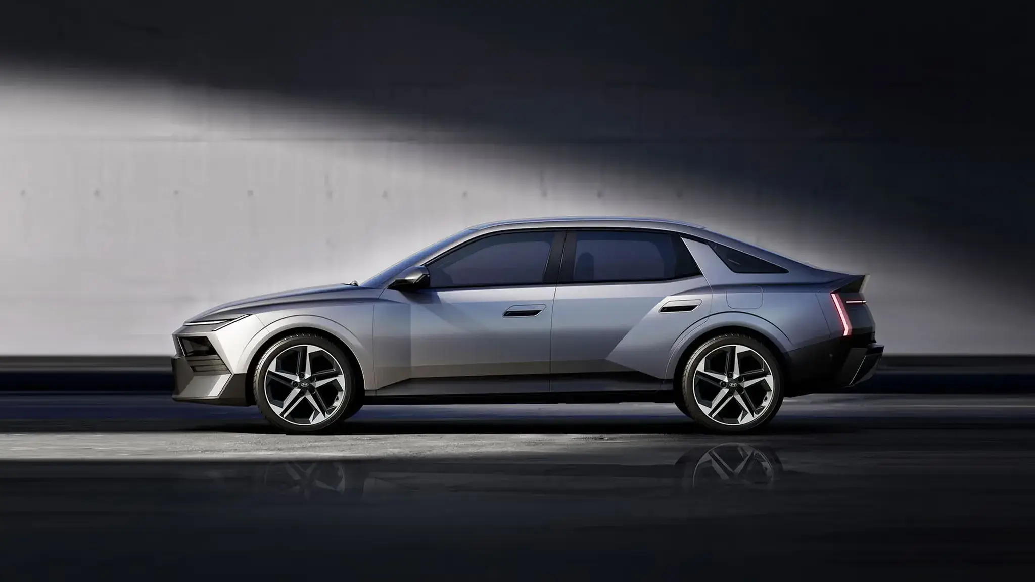 Silver-gray 2027 Hyundai Elantra sedan in side profile with five-spoke alloy wheels, flush door handles, a triangular rear quarter window and a vertical taillight, in a dark studio with a diagonal beam of light