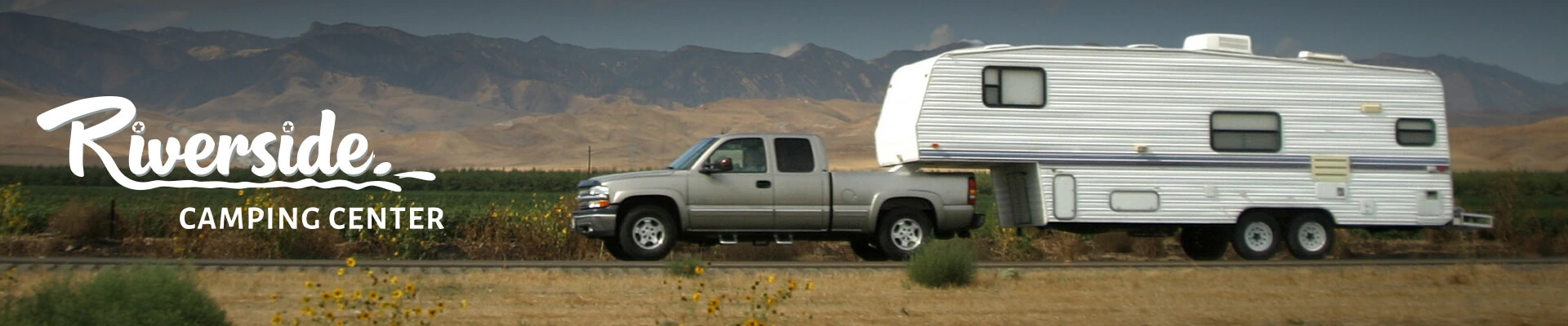 A wide angle action shot of a truck towing a large fifth wheel camper down a remote rural road.