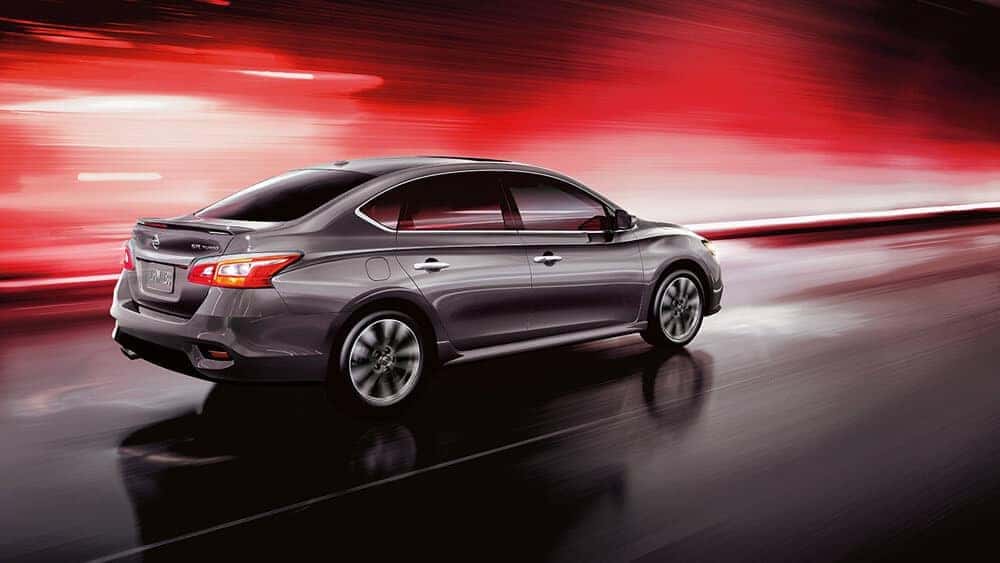 Gray 2018 Nissan Sentra sedan driving past a red-lit wall