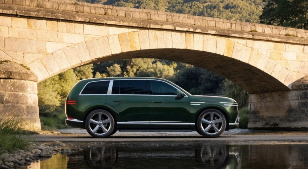 Side view of a green 2027 Genesis GV90 parked by a river bridge.