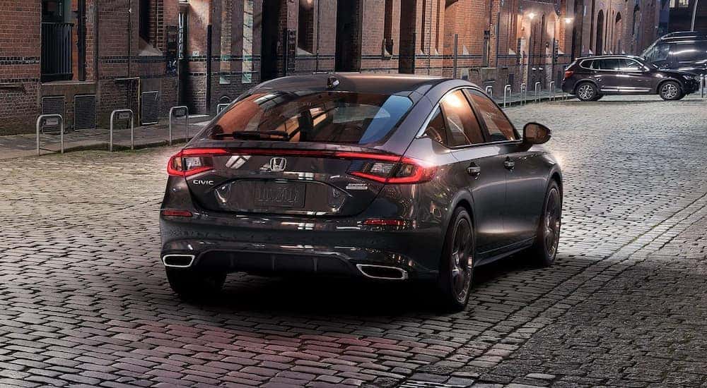 A grey 2024 Honda Civic Hatchback Sport Touring is driving on a cobblestone street.