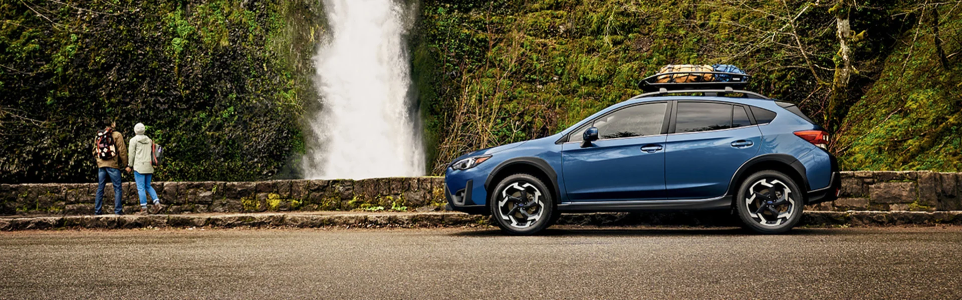Subaru Crosstrek with roof cargo parked near a waterfall with hikers