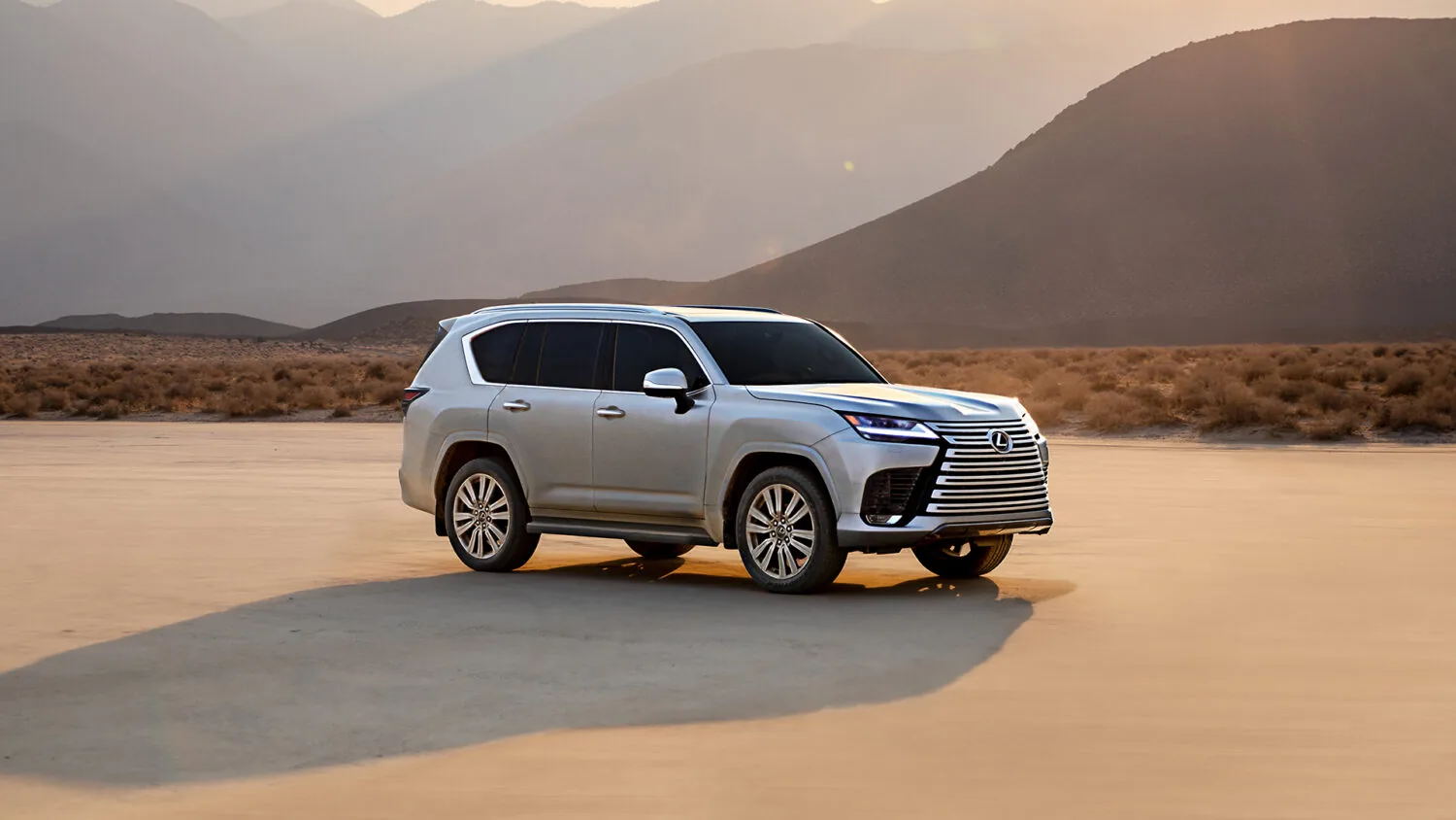 Point-of-view from the driver's seat of a Lexus showing hands on the steering wheel with the Lexus logo, a digital speedometer reading 60 mph, and an infotainment screen displaying a music playlist, with a sunset over a winding road ahead.