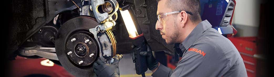 Nissan service technician inspecting a brake rotor and caliper with a work light