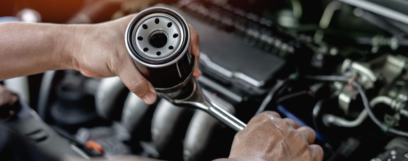 A close up shows a mechanic holding a black oil filter and socket wrench.