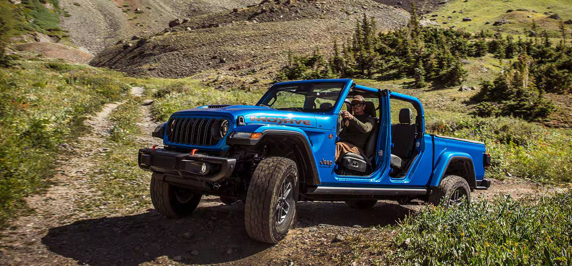 A blue jeep driving on a dirt path.