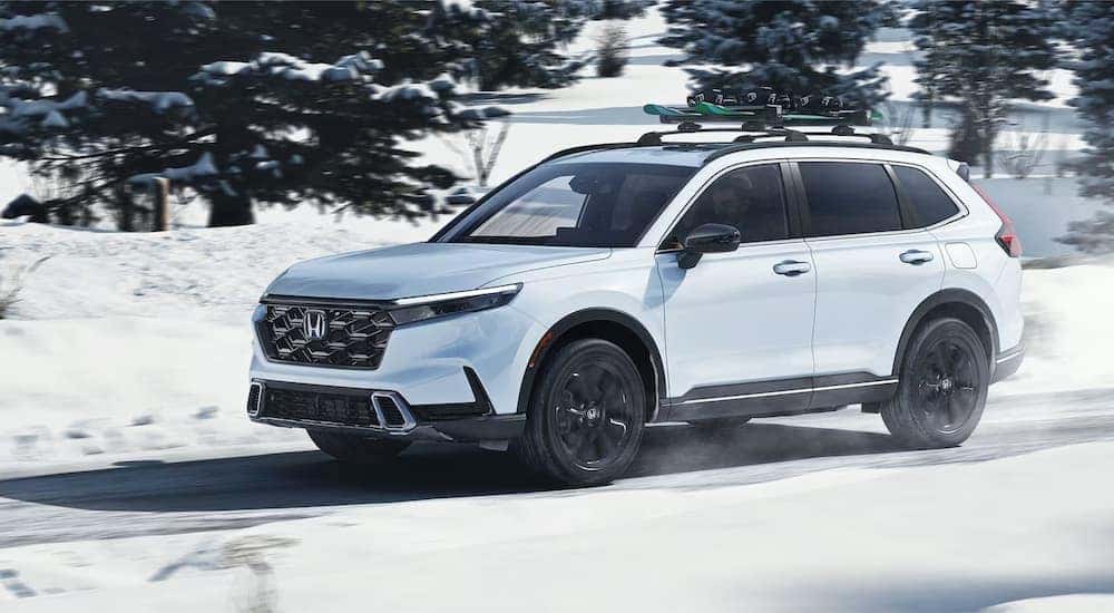 White 2025 Honda CR-V Sport Touring Hybrid driving down a snowy road.